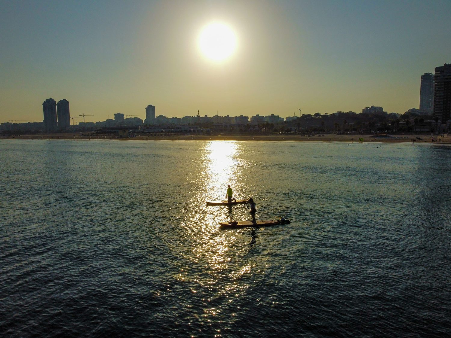 Dos personas en paddle surf con el reflejo del sol sobre el agua