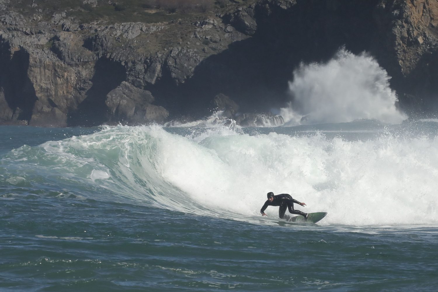 Surfista recortando con gran salpicadura frente a acantilados