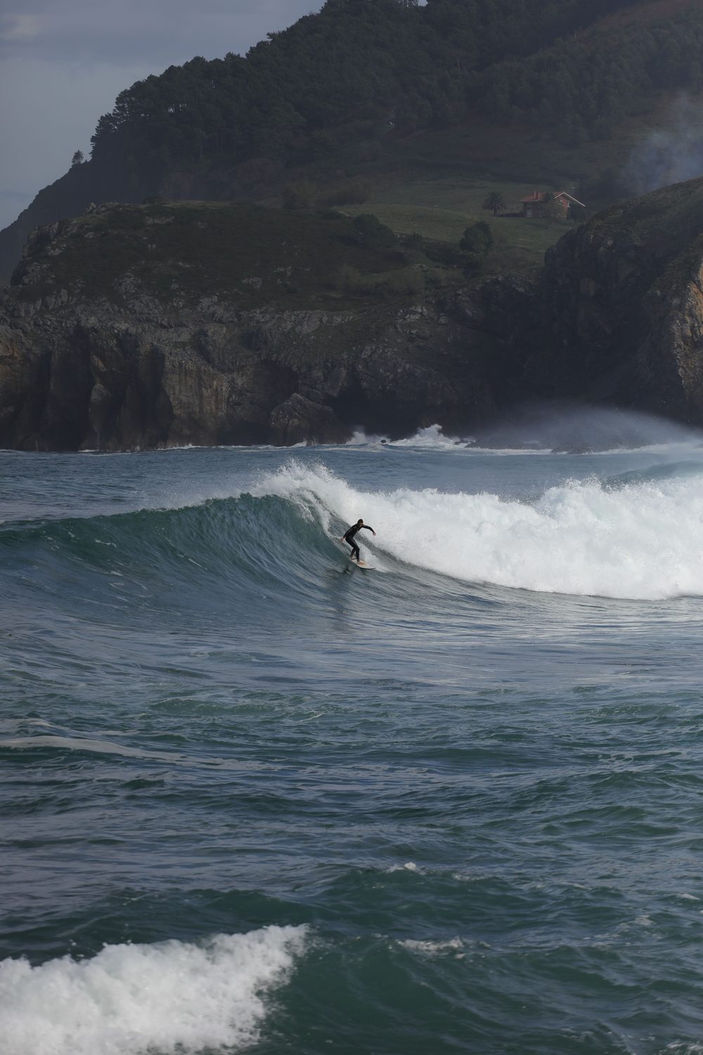 Surfista en una ola con acantilados verdes al fondo